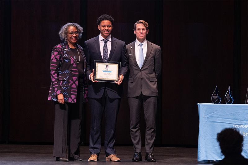 A student, Michael Fair, taking a group photo with two other people on stage, Lee H. Roberts and Leah Cox, after winning an award.