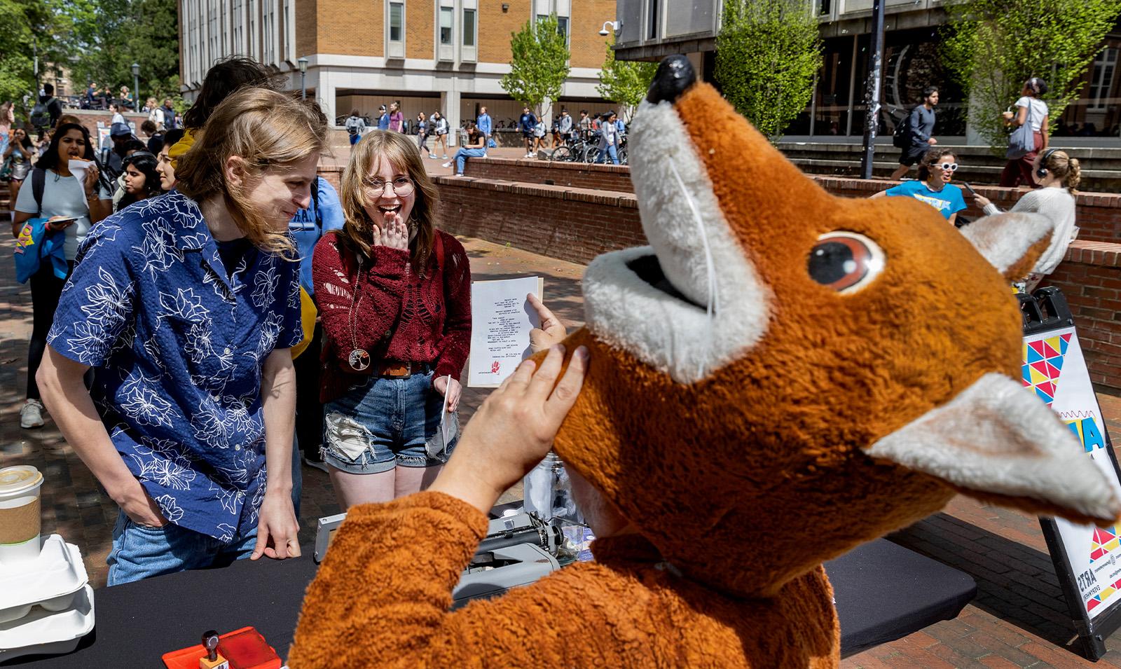 A man in a fox costume, known as the poetry fox, reading a poem he wrote to people standing in line.