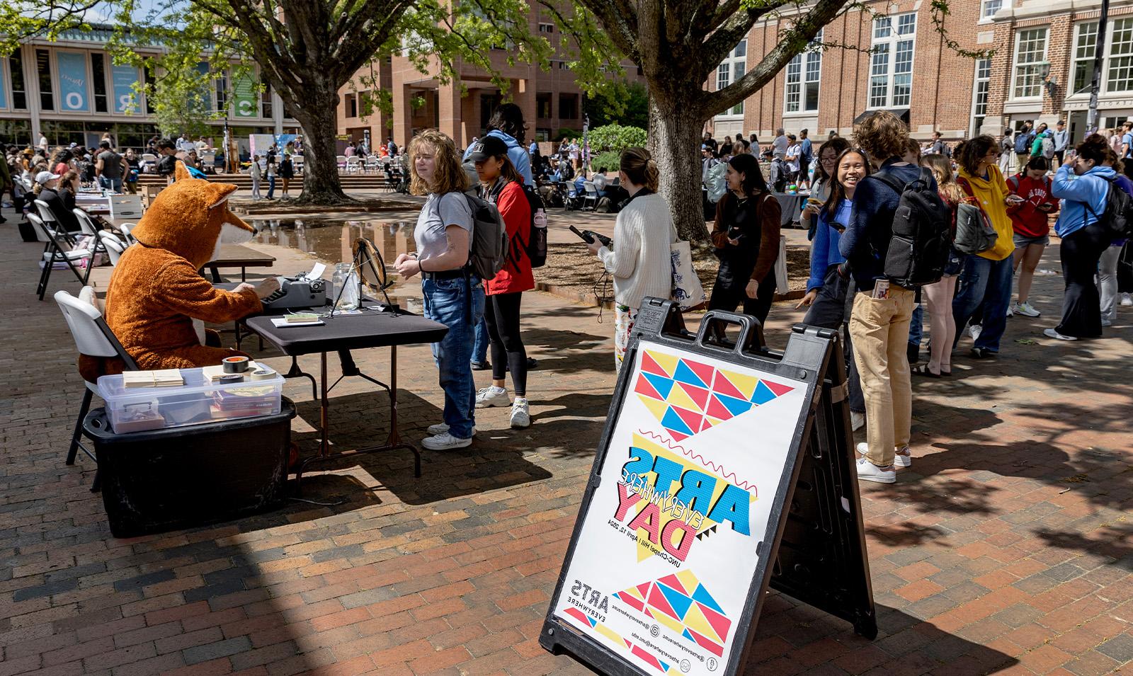 A line of people waiting to receive a poem from the Poetry Fox. A sign advertising 