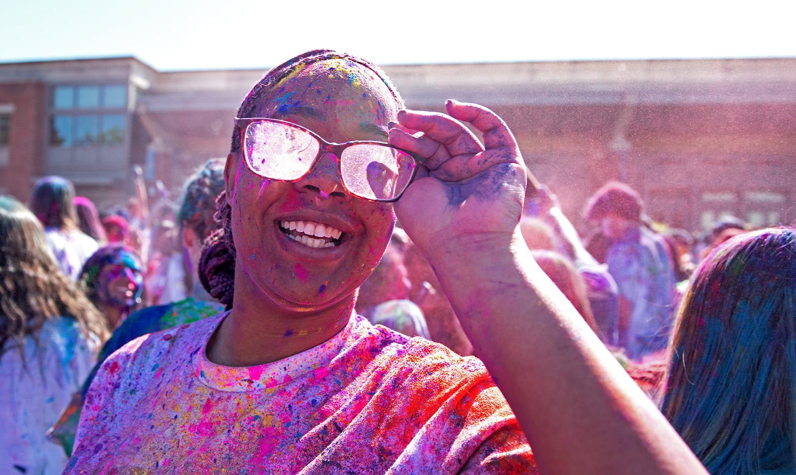 A student covered in paint celebrating Holi and smiling for a photo.