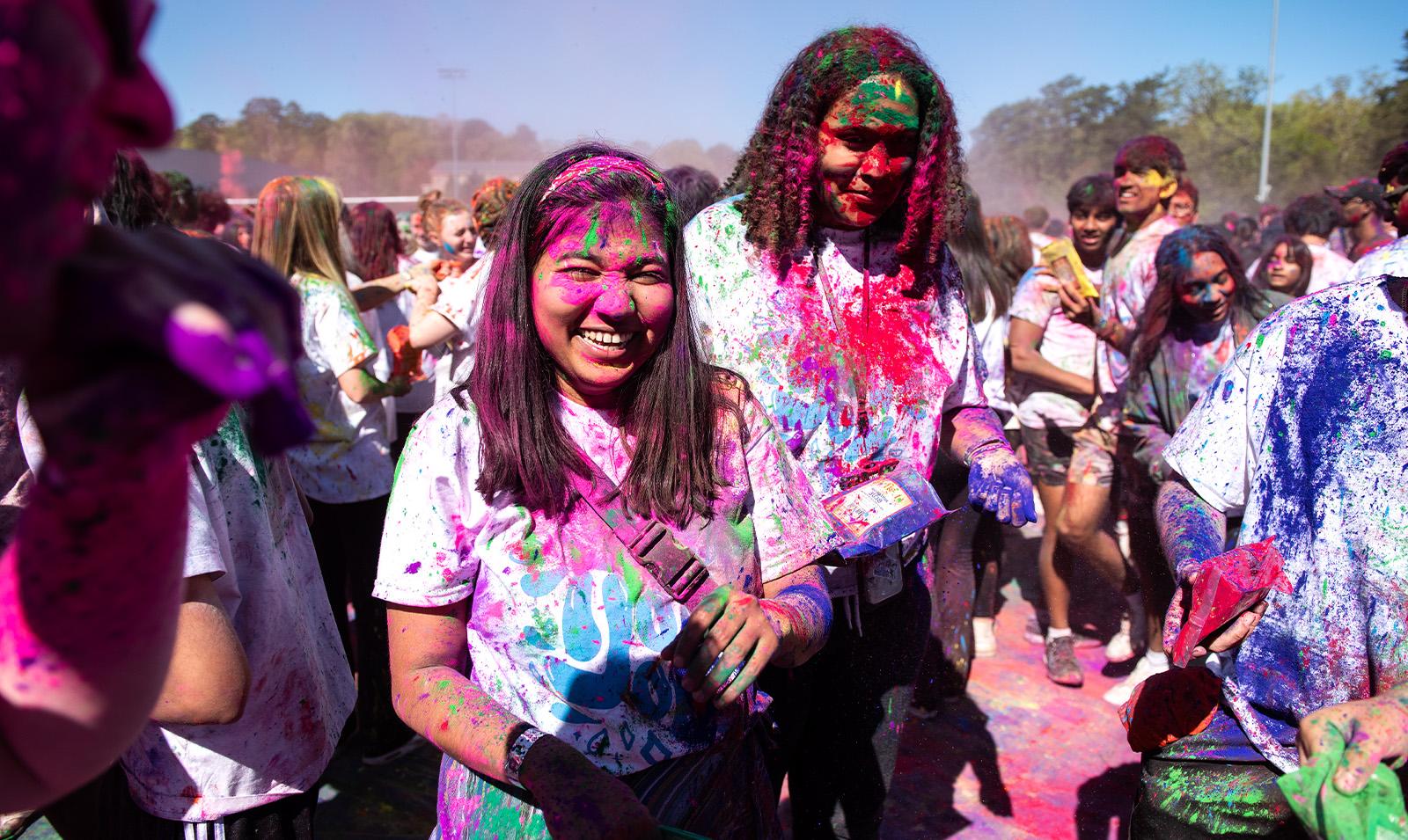 Two students covered in paint celebrating Holi.