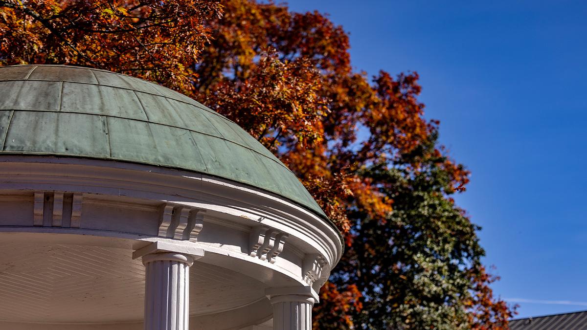 Dome and pillars of the Old Well with fall-time orange and red leaves seen in the background.