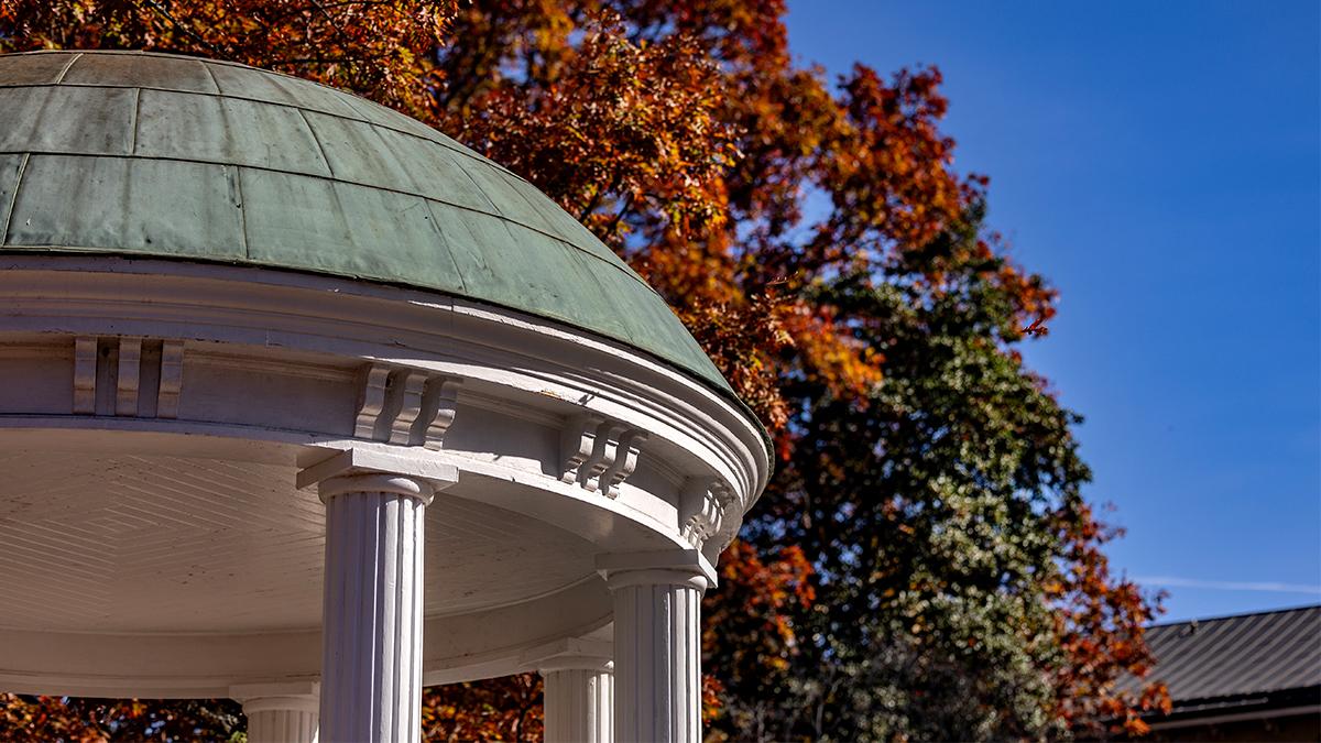 Close-up image of the Old Well on a sunny fall day on the campus of UNC-Chapel Hill with trees with orange leaves seen in the background.